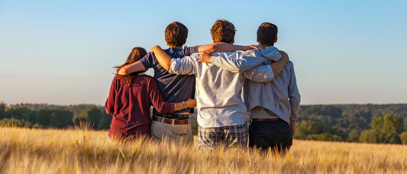 Four young people embracing and supporting one another on a grass field.